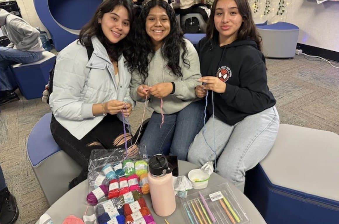 Three students crocheting together at a table in the Wellness Center.